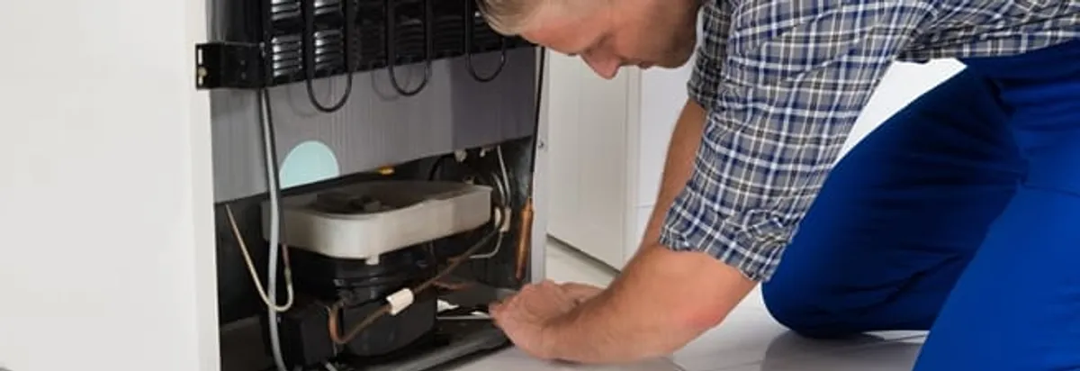 Refrigerator repair technician servicing the compressor and condenser area in Fort Wayne, IN